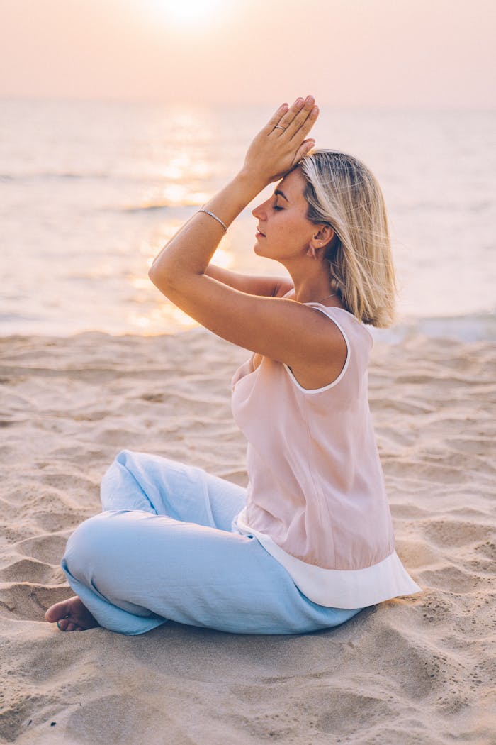 A woman meditates at sunrise on a serene beach, embracing mindfulness and relaxation.