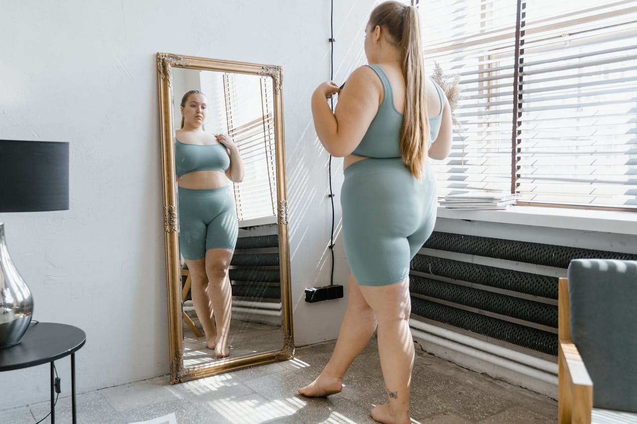 Plus size woman in activewear admiring her reflection in a mirror indoors.